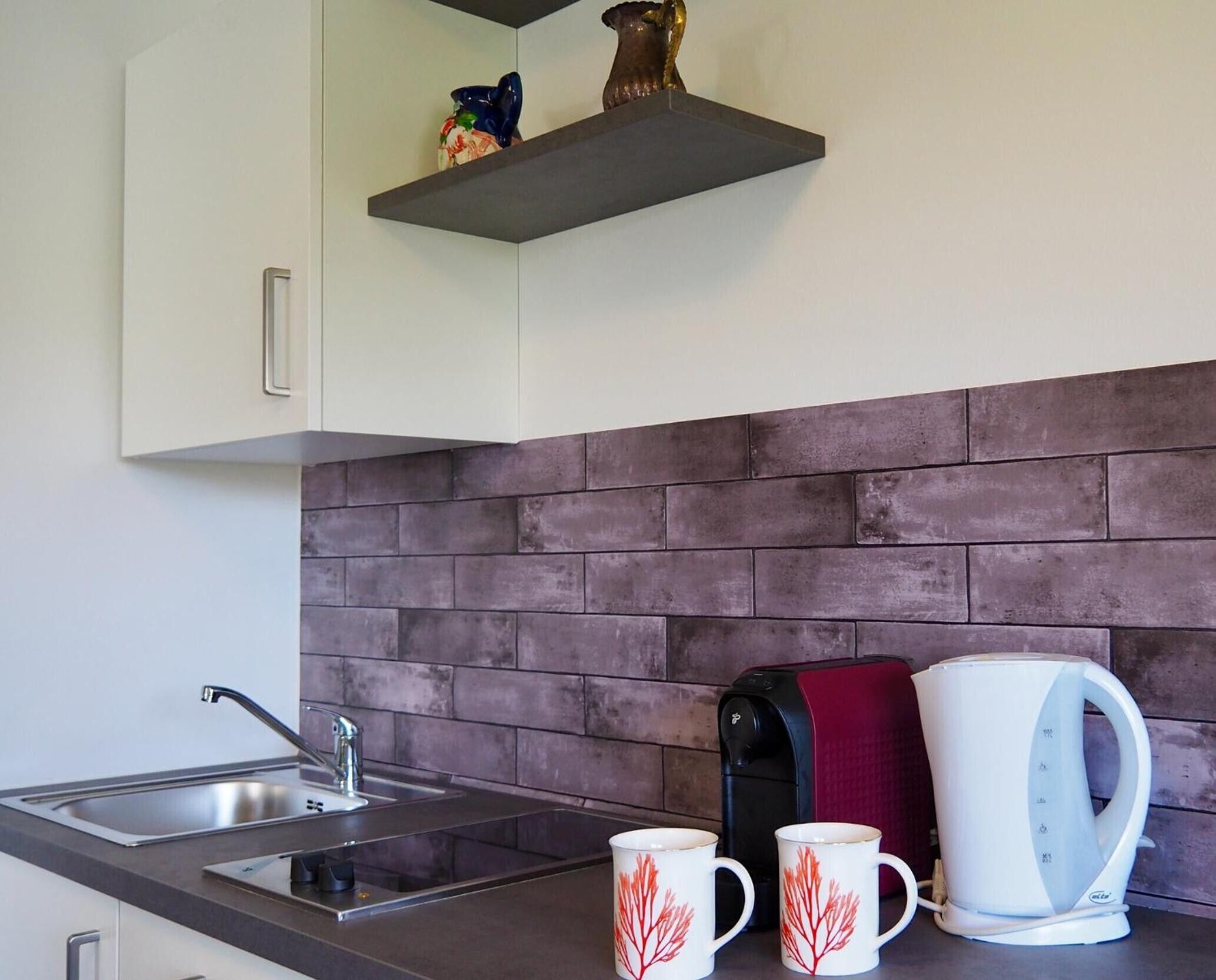 Una cocina de diseño moderno, con un rebozado de ladrillo, un lavamanos de acero inoxidable y una cafetera.