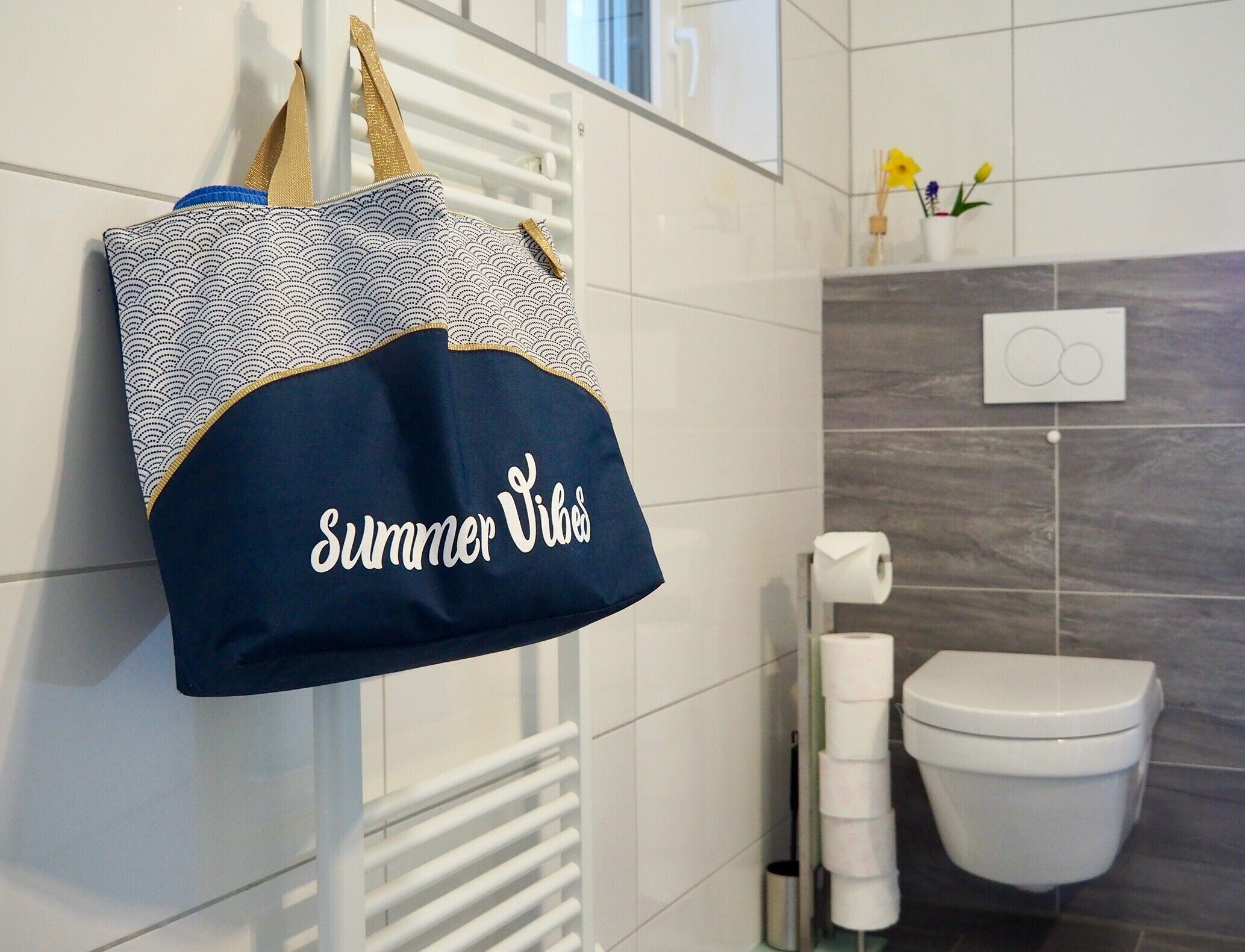 Een badkamer met een handdoekhouder, een decoratieve tas, een toilet en een lichtschakelaar aan de muur.