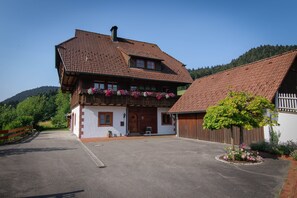 A traditional wooden house with a sloped roof, a front porch with flower boxes, and a paved driveway.