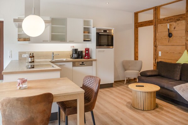 A modern kitchen with a coffee maker, a microwave, and a sink. There is a dining area with a table and chairs.