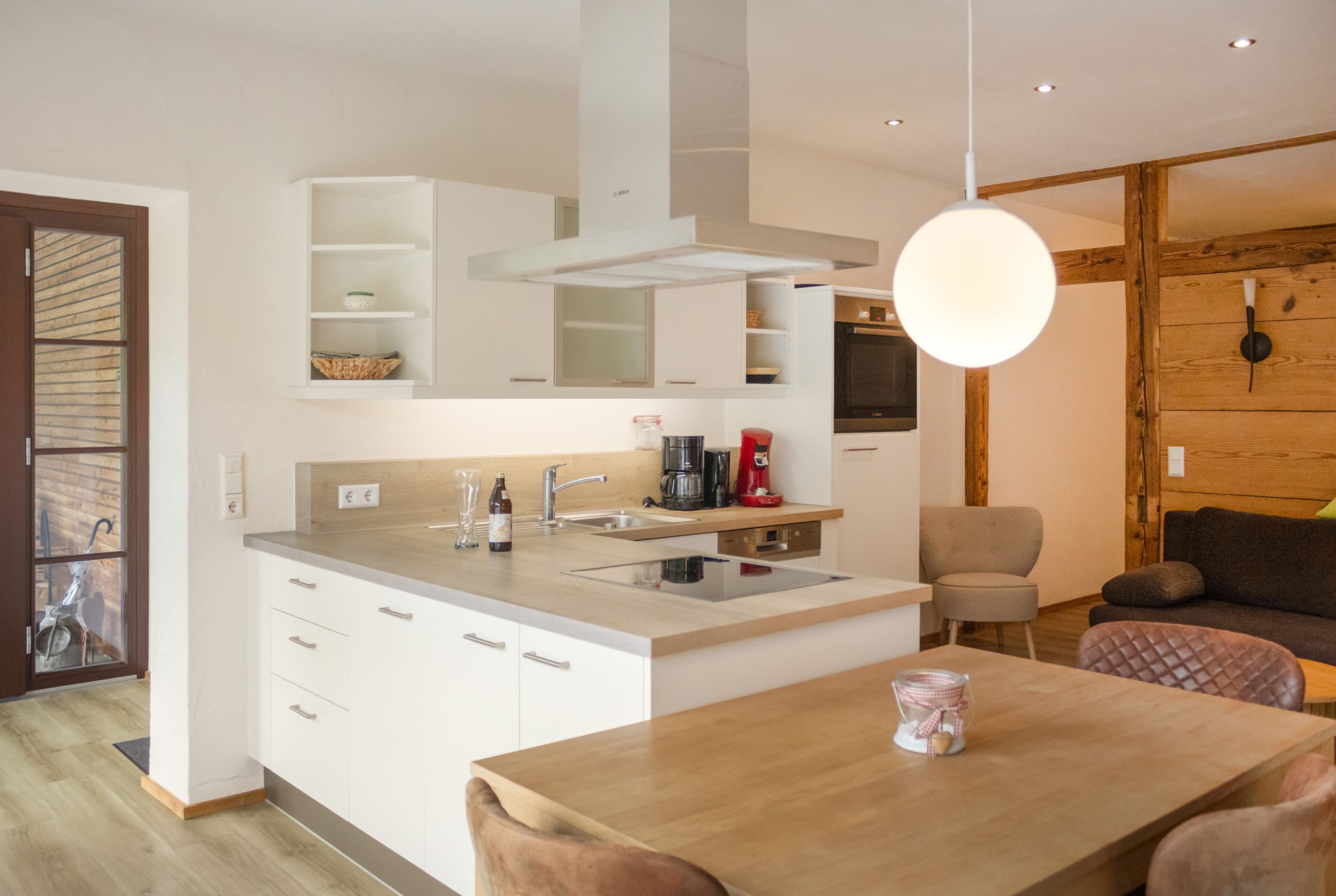 Una cocina moderna con armarios blancos, una isla central y un comedor con mesa de madera.