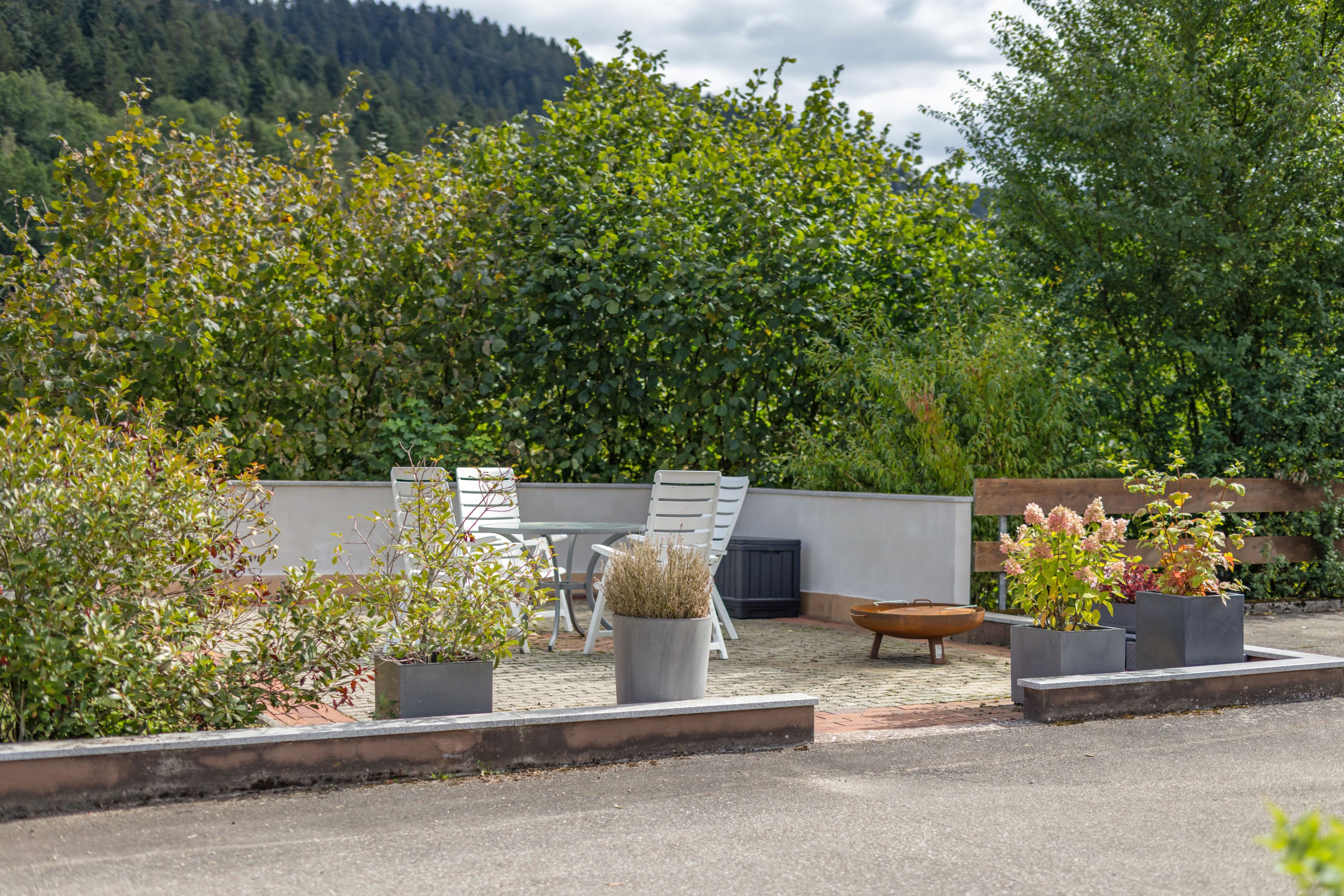 An outdoor seating area with a table and chairs, surrounded by potted plants and a decorative fire bowl.
