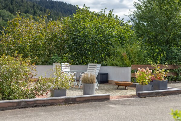An outdoor seating area with a table and chairs, surrounded by potted plants and a decorative fire bowl.
