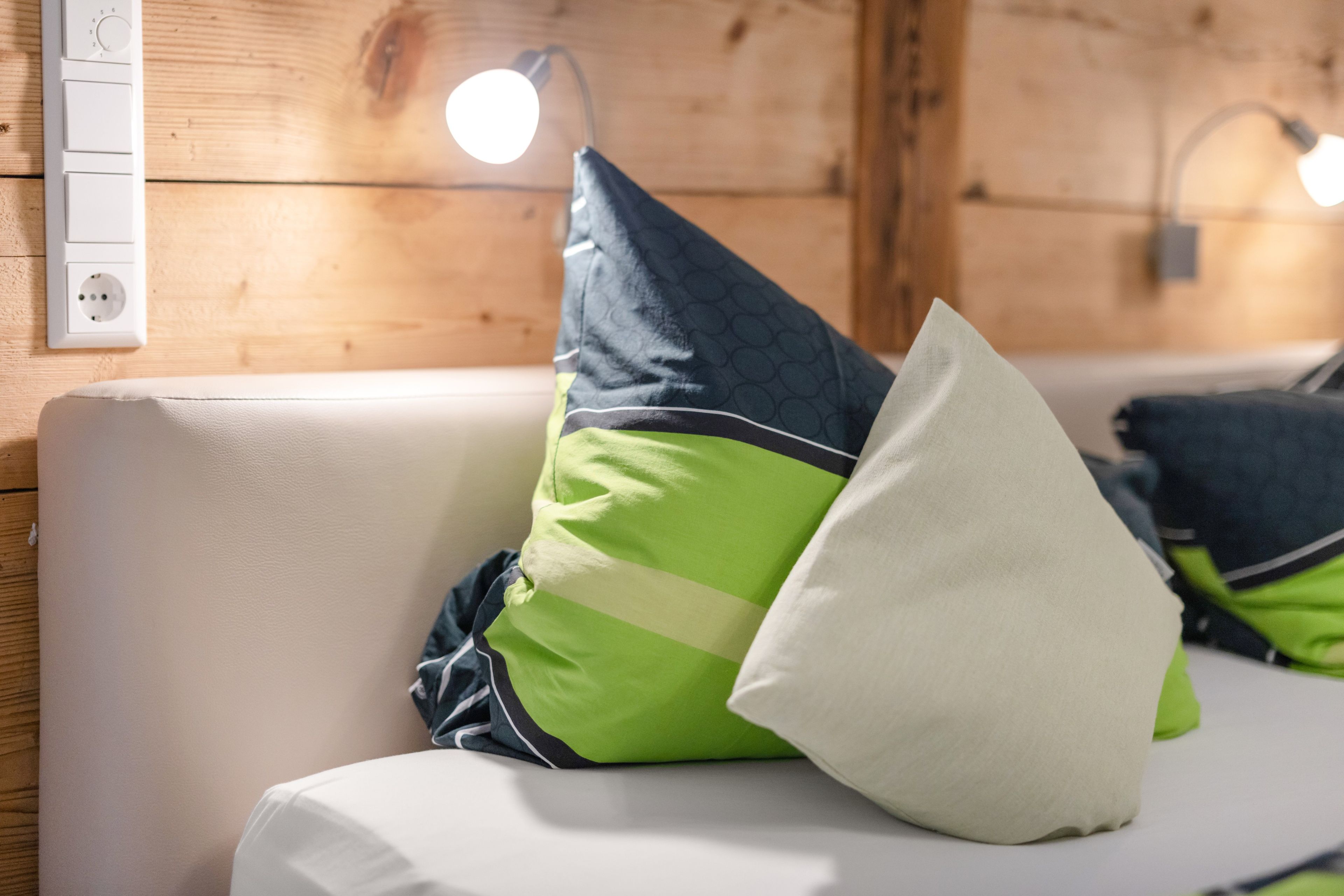 Un interior de madera con un sofá blanco, cojines verdes y blancos, y un enchufe de pared.