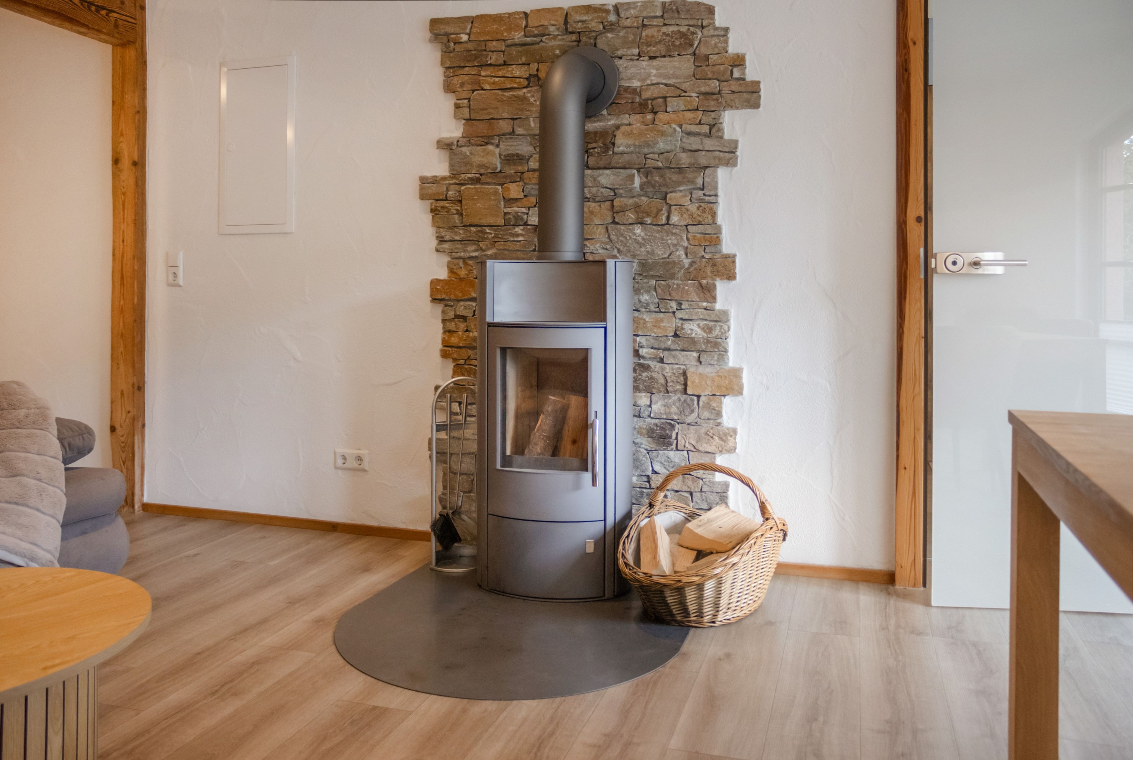 A modern living room with a stone wall, a built-in wood stove, and a wicker basket on the floor.