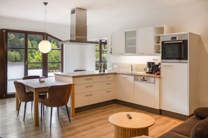 A modern kitchen with a dining area, wooden flooring, and large windows.