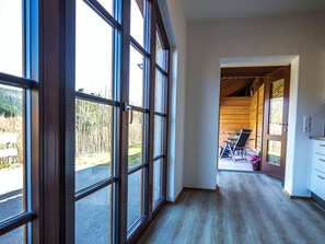 A hallway with large windows, a wooden floor, and a view of outdoor seating.