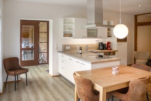 A modern kitchen with a central island, white cabinetry, and a dining area with brown chairs.
