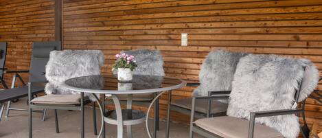 A round metal table with two chairs, each with a fur throw. A small potted plant with pink flowers is on the table.