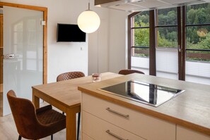 A modern kitchen with a wooden table, two chairs, a built-in oven, and a large window with a view of greenery.