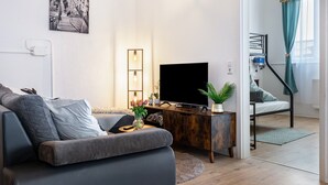 A modern living room with a sofa, a flat-screen TV, a wooden cabinet, and a staircase leading to an upper floor. - Holiday Apartment 'Mäxle's Loft' with Shared Garden and Wi-Fi (Fluorn-Winzeln)
