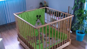 A wooden crib with a green polka-dotted mattress and a bear design, placed in a room with wooden flooring and a blue potted plant. - Apartment 'Schopper' with Balcony and Wi-Fi (Halblech)
