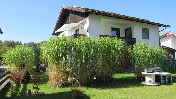 A two-story house with a sloped roof, a satellite dish, and a small garden with tall grass. - Apartment 'Schopper' with Balcony and Wi-Fi (Halblech)