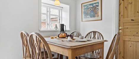 A dining area with a wooden table and chairs, a window with a view of a brick building, a painting on the wall, and a door with a wooden panel.