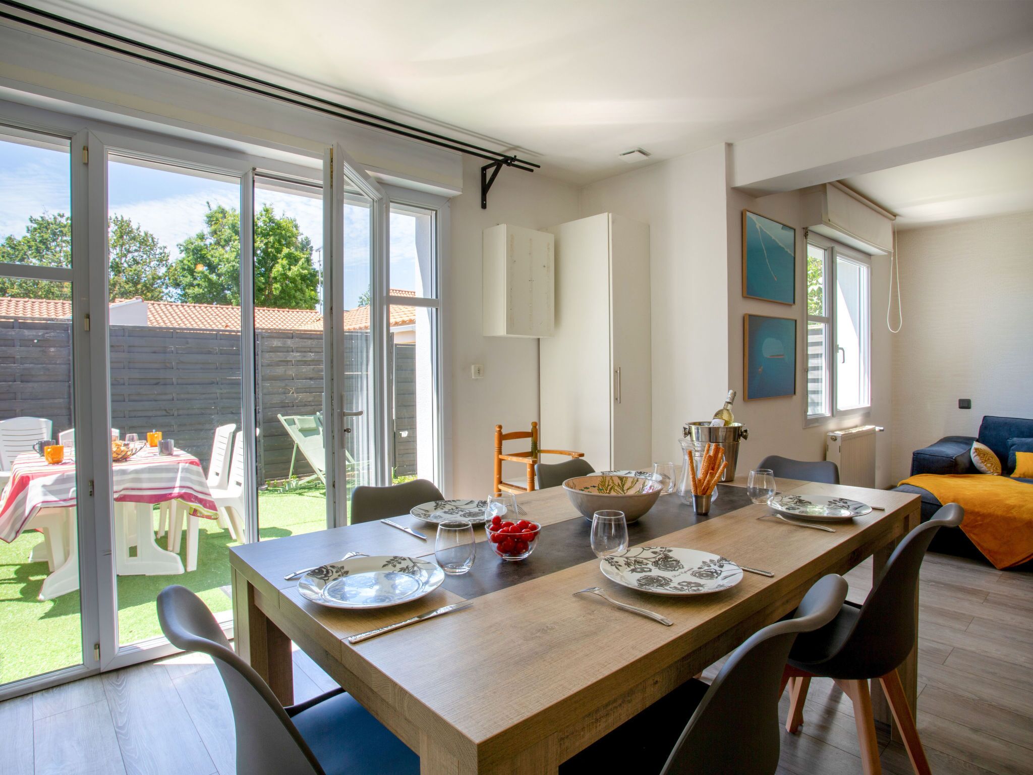 Un comedor con mesa de madera dispuesta para cuatro personas, un ventanal y vista al jardín.