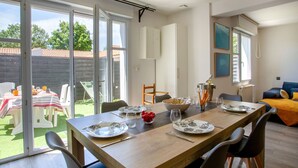 A dining area with a wooden table set for four, a large window, and a view of the garden. - Les Matelos by Interhome (Pornic)