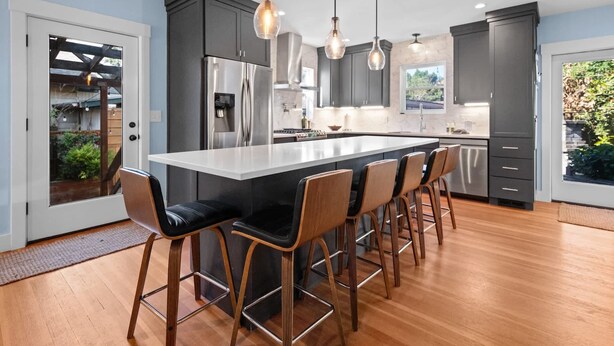 Uma cozinha moderna com ilha central, banquetas, eletrodomésticos de aço inoxidável e iluminação pendente.