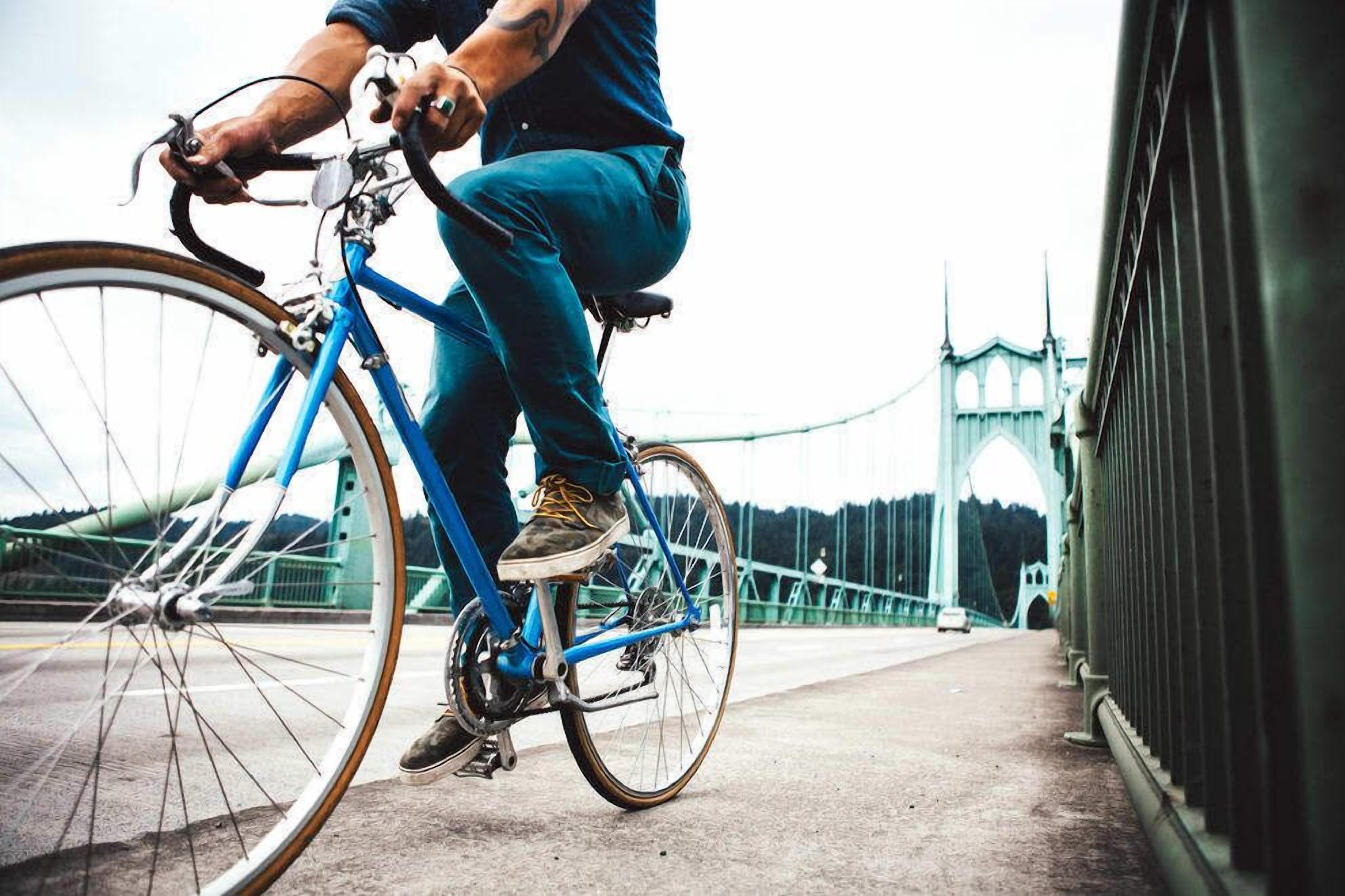 Eine Person fährt ein blaues Fahrrad über eine Brücke, im Hintergrund eine große Bogenkonstruktion.