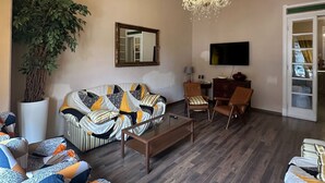 A living room with a sofa, armchairs, a coffee table, a chandelier, a television, and a large potted plant. - Viareggio Old Style Sea View (Viareggio)