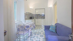 Un espace de vie compact comprenant un coin cuisine, un coin repas avec une table et des chaises, et un canapé avec un coussin.
