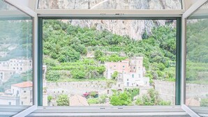 Une pièce dotée d’une grande fenêtre donnant sur une colline, avec des bâtiments et de la végétation.