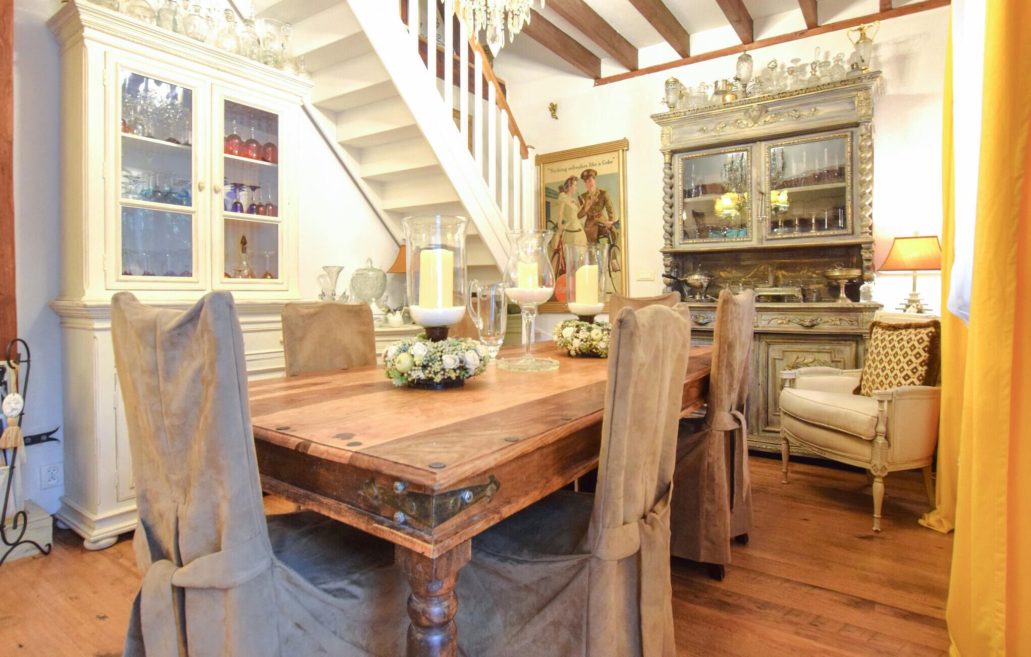 Une salle à manger avec une table en bois, des chaises, un lustre et un escalier.
