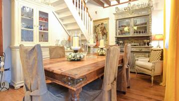 Une salle à manger avec une table en bois, des chaises, un lustre et un escalier.