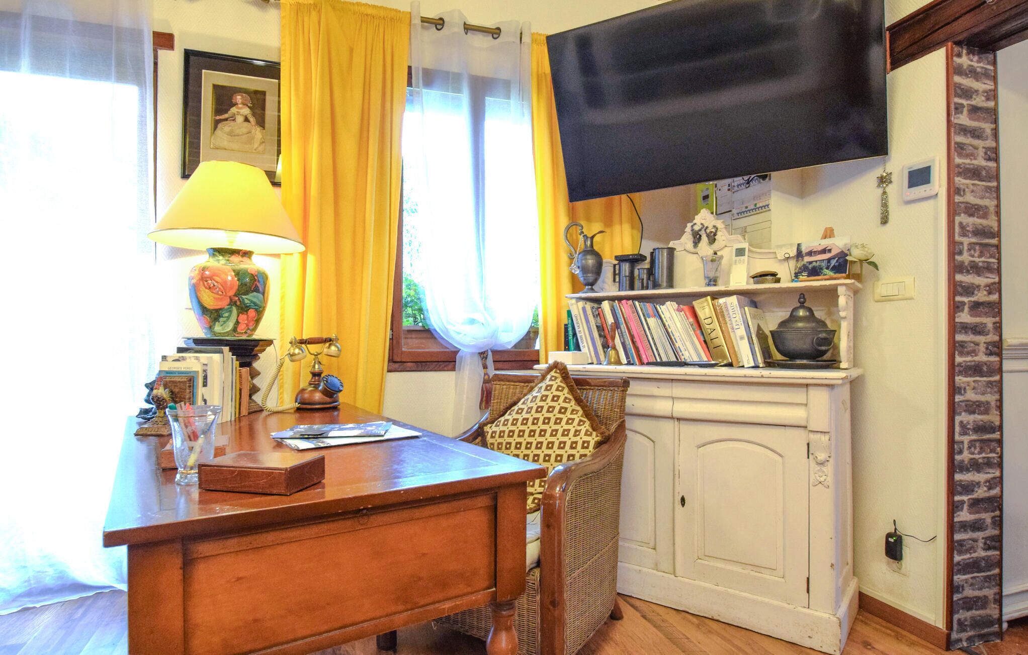 Een gezellige kamer met een houten bureau, een lamp, een boekenplank en een televisie aan de muur.