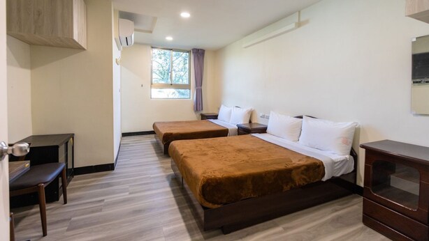 A hotel room with two beds, a desk, a dresser, and a window with curtains. - Green Field Mountain Villa (Taoyuan City)