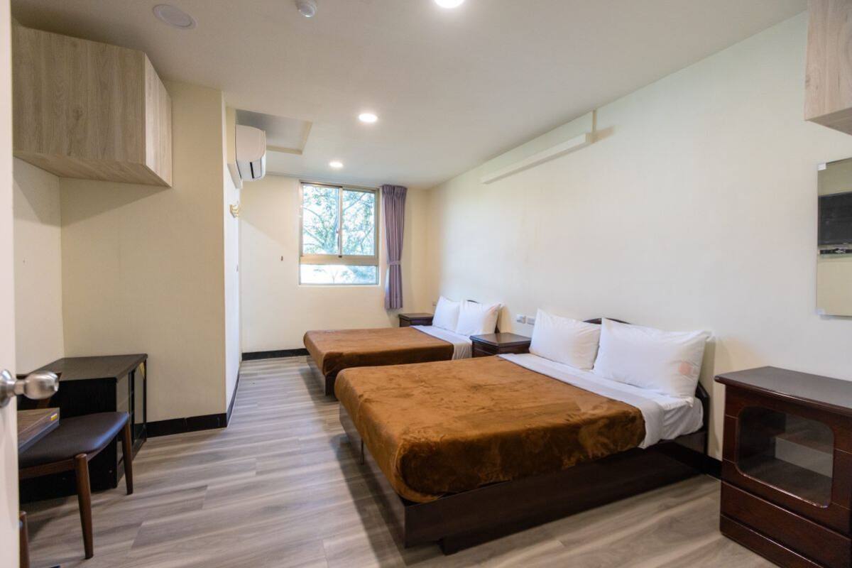 Habitación de hotel con dos camas, un escritorio, un tocador y una ventana con cortinas.