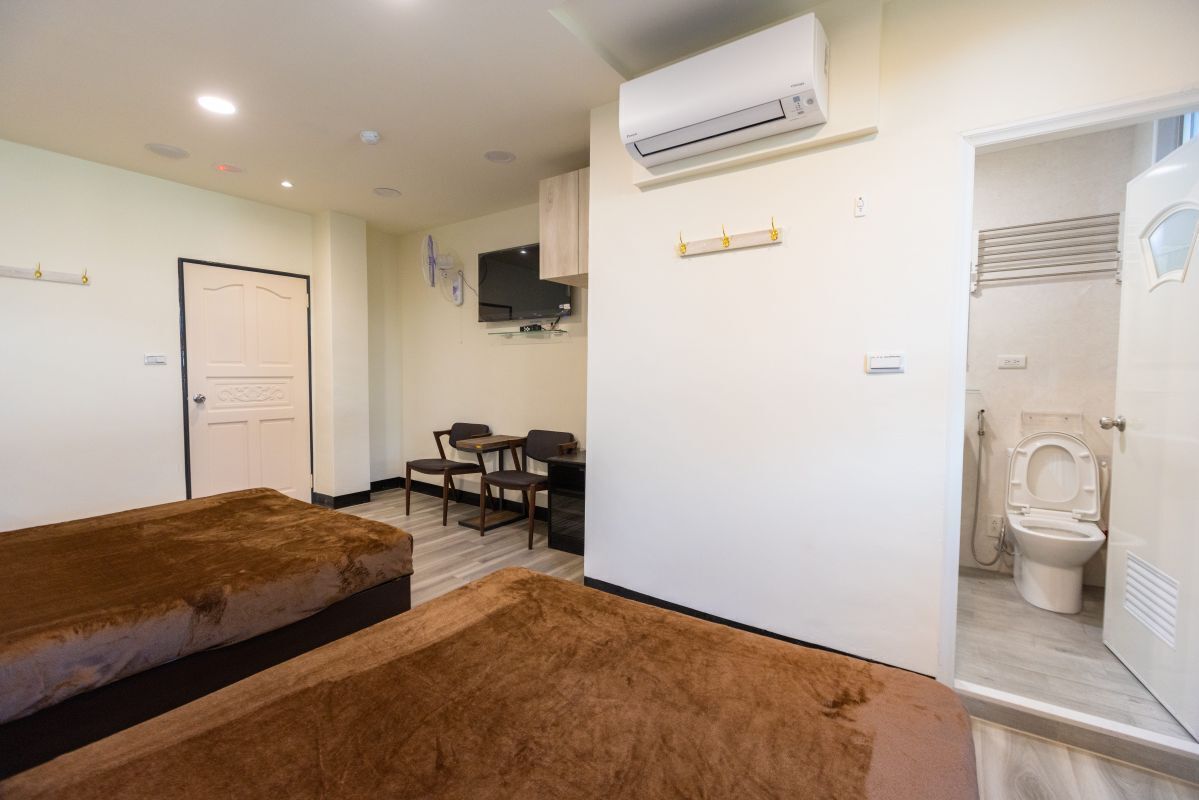 A compact room with a bed, a small table, and a chair. There is a toilet and a sink visible.