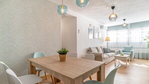Ein modernes Wohnzimmer mit einem Holzesstisch, hellen Sofas und einem großen Fenster mit durchsichtigen Vorhängen.