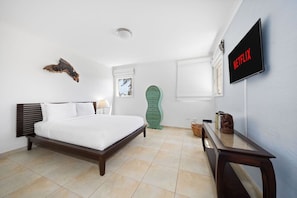 Un dormitorio con cama, cómoda verde, mesita de noche de madera, televisor y una obra de arte colgada en la pared.