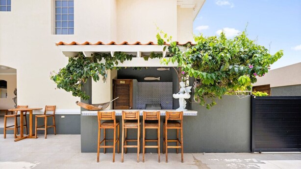 Une terrasse extérieure avec une table et des chaises, un petit coin salon et un mur orné d’une sculpture de poisson décorative.