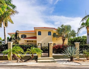 Una casa de dos pisos con tejado de tejas rojas, fachada color beige y entrada con portón.