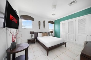 Ein modernes Hotelzimmer mit Bett, Wand-Fernseher, kleinem Tisch und Nachttisch.
