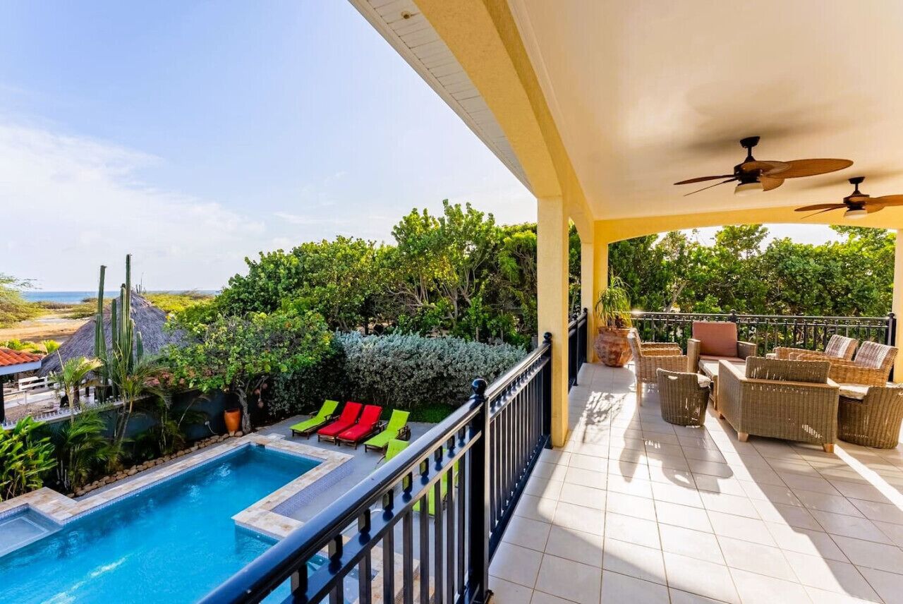 Ein Poolbereich mit Meerblick, Liegestühle und eine überdachte Terrasse mit Korbmöbeln.