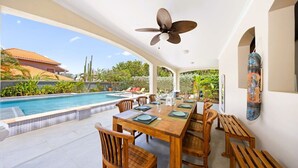Un espacio de comedor al aire libre cubierto con piscina, mobiliario de madera y ventilador de techo.