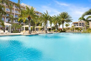 Ein großer Pool mit Liegestühlen und Palmen, umgeben von Hotelgebäuden.