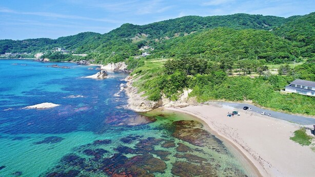 Zona costera con playa, aguas claras y colinas verdes.