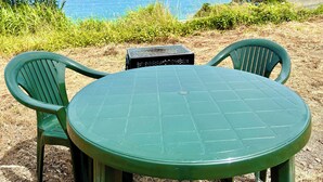 Una mesa verde y dos sillas sobre un césped con vista al océano.