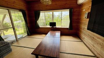 Een kamer met houten inrichting, een tatami vloerbedekking, een tafel, een televisie en een raam met gordijnen.