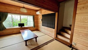 Una habitación japonesa tradicional con suelo de tatami, una mesa de madera baja, un televisor y una ventana con cortinas.