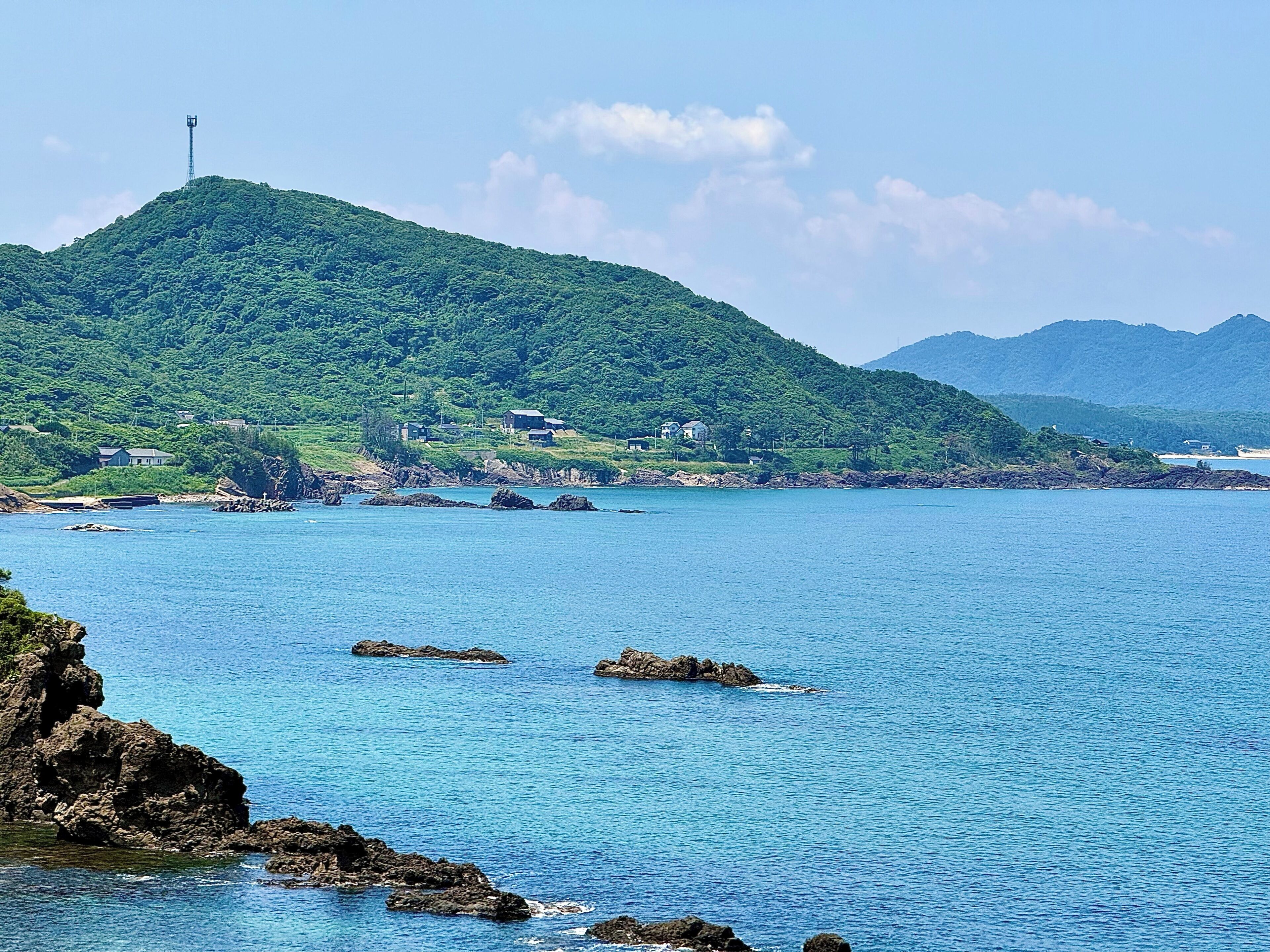 A coastal landscape with a hill, rocky shoreline, and a few buildings.