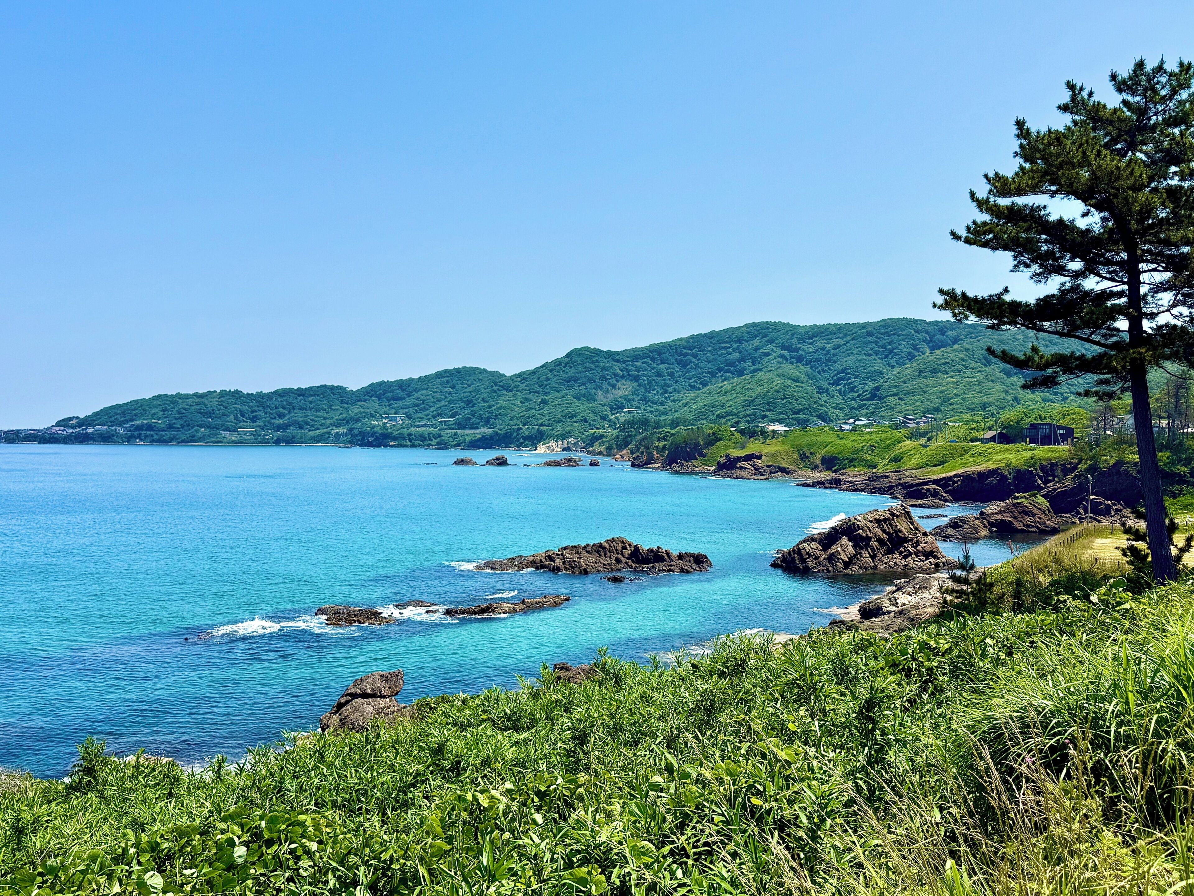 A coastal landscape with clear blue waters, rocky outcrops, and lush greenery.
