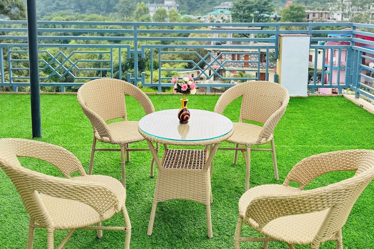 A terrace with wicker furniture and a glass table, overlooking a green landscape and distant buildings.