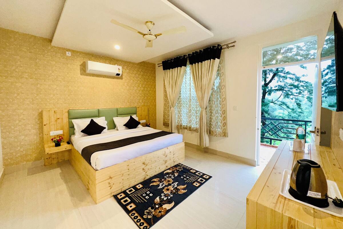A bedroom with a bed, a ceiling fan, a window with curtains, a wooden nightstand, and a coffee maker on the dresser.