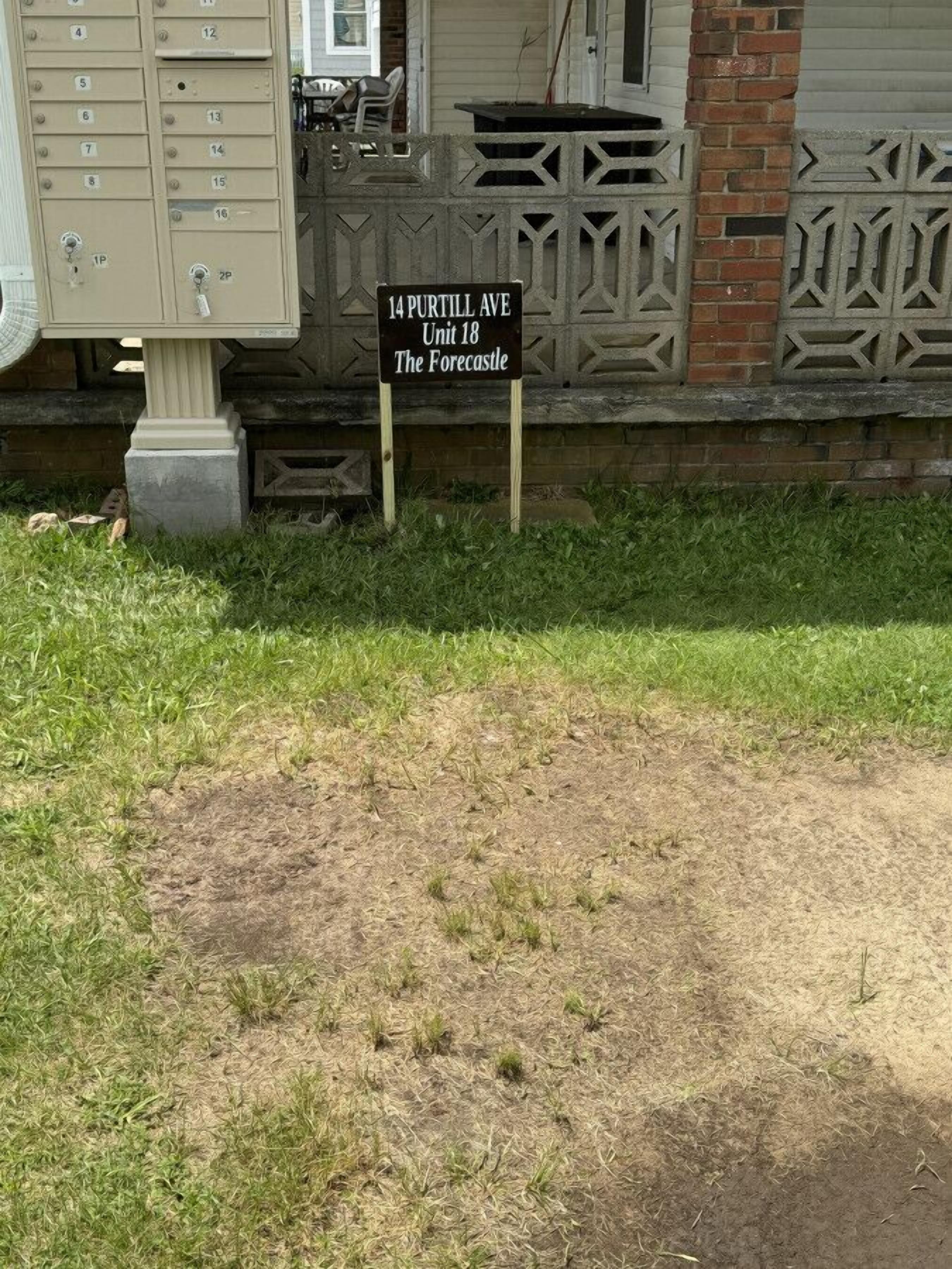 Señal de 14 Purill Ave, Unidad 18, The Forecastle, con un buzón y un muro de ladrillo al fondo.