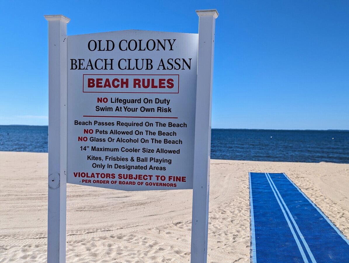 A beach sign with rules for Old Colony Beach Club Assn, including no lifeguard on duty, no pets, no glass or alcohol, and a 14" maximum cooler size allowed.