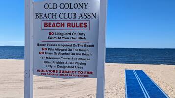 A beach sign with rules for Old Colony Beach Club Assn, including no lifeguard on duty, no pets, no glass or alcohol, and a 14" maximum cooler size allowed.